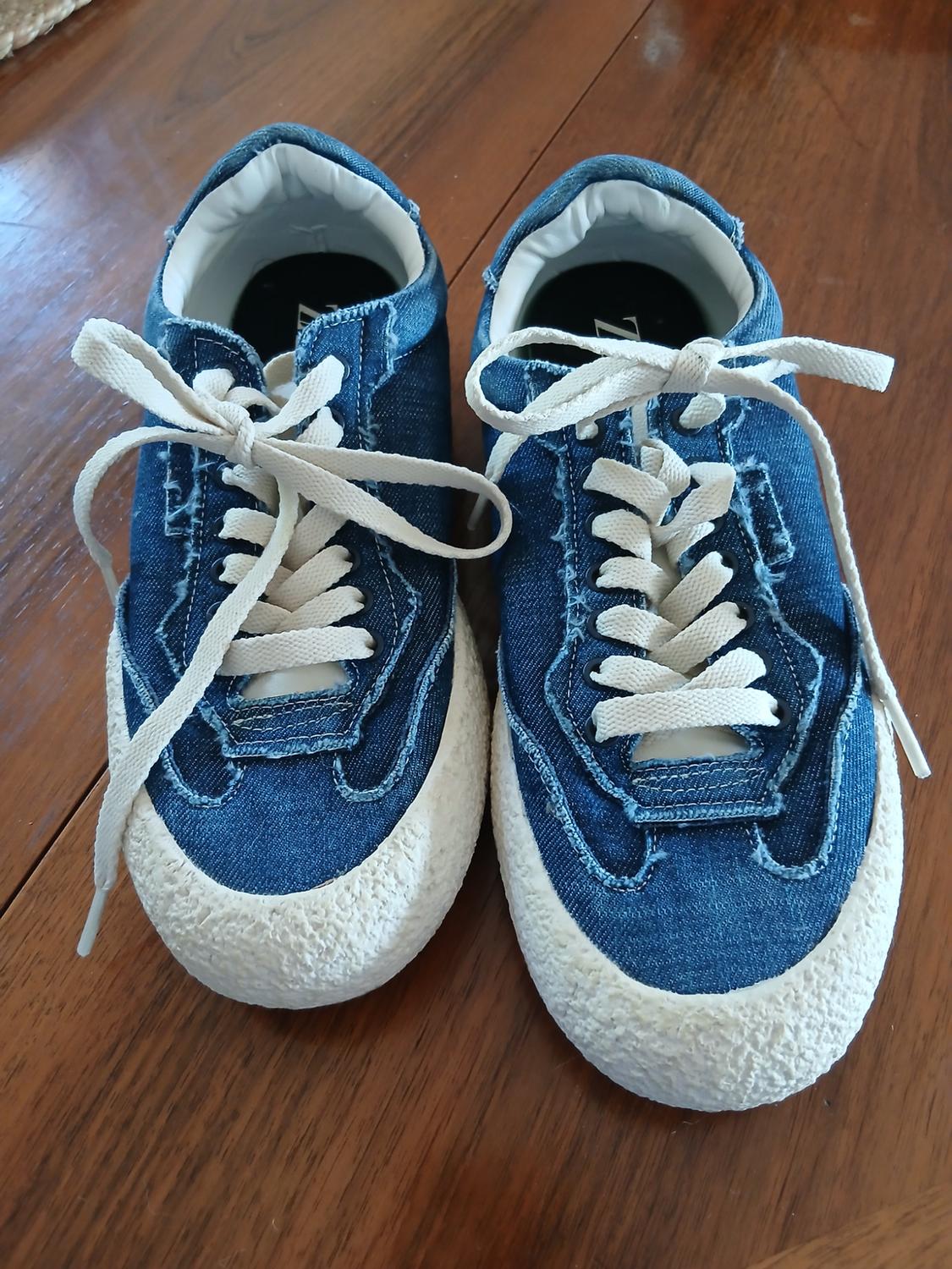 Front view of blue denim trainers with white laces and a textured sole.