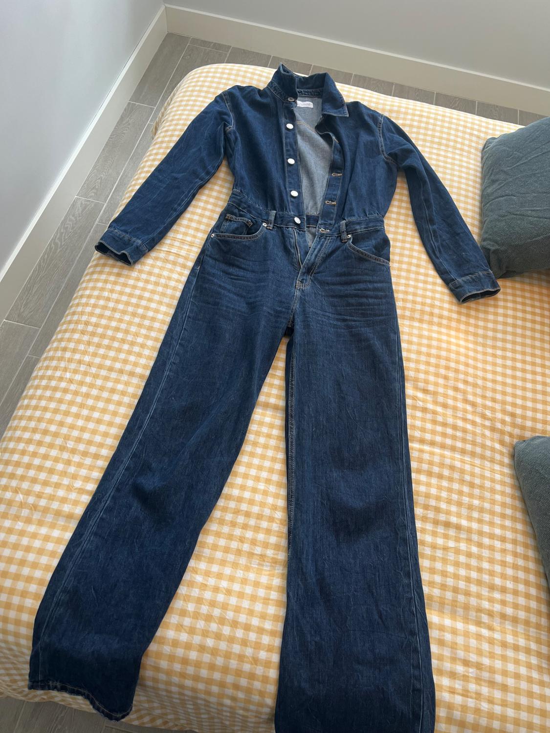 Dark blue denim dungarees with white buttons, spread out on a bed with a yellow and white checked bedspread.