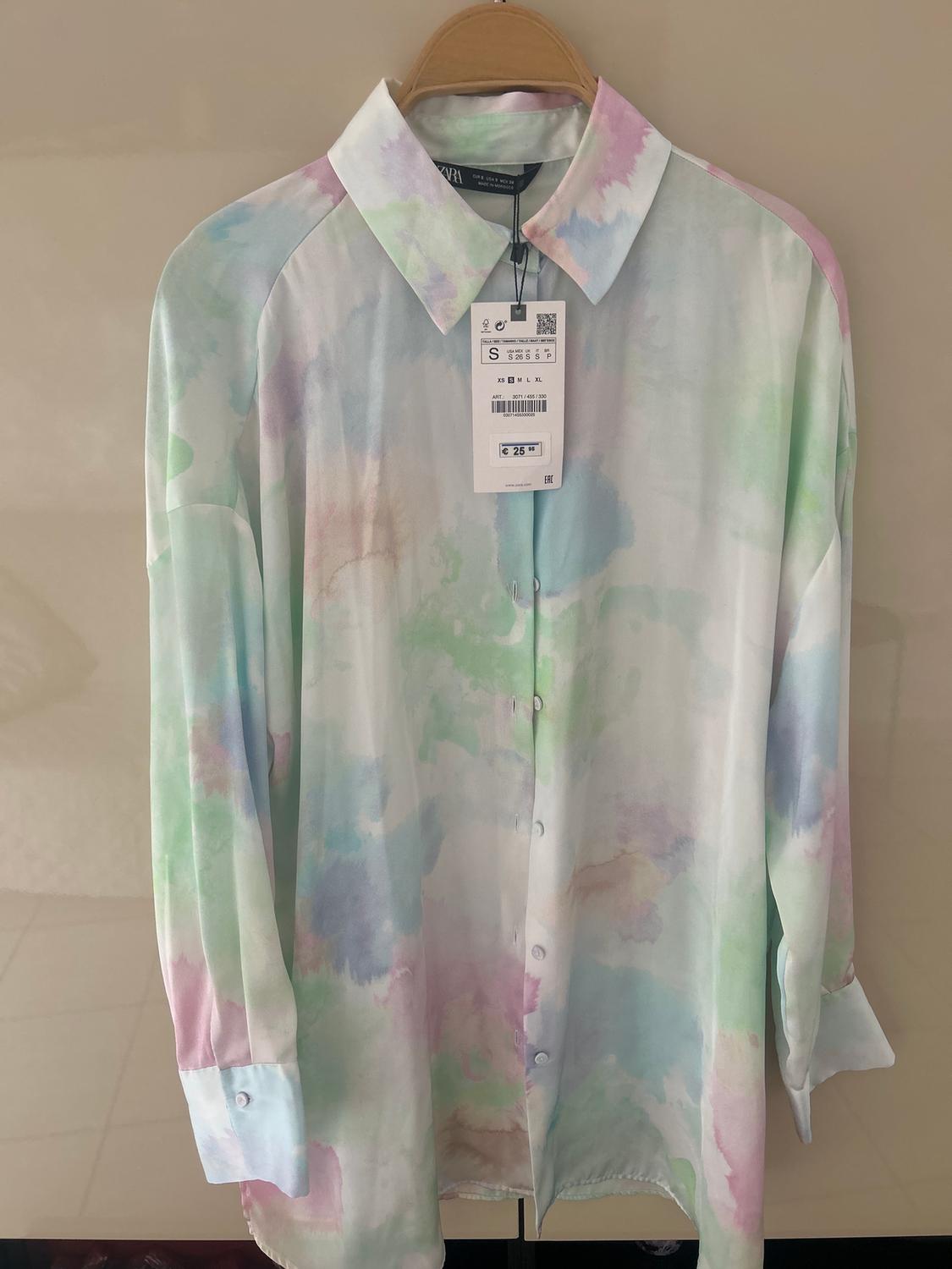 Long-sleeved shirt with a watercolour pastel print, hanging on a hanger. Visible tag with a price of €25.