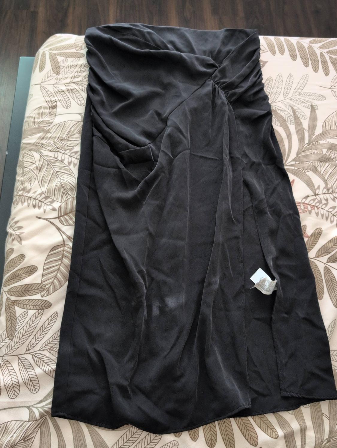 Long black skirt with draping and a side slit, on a bed with botanical-print sheets.