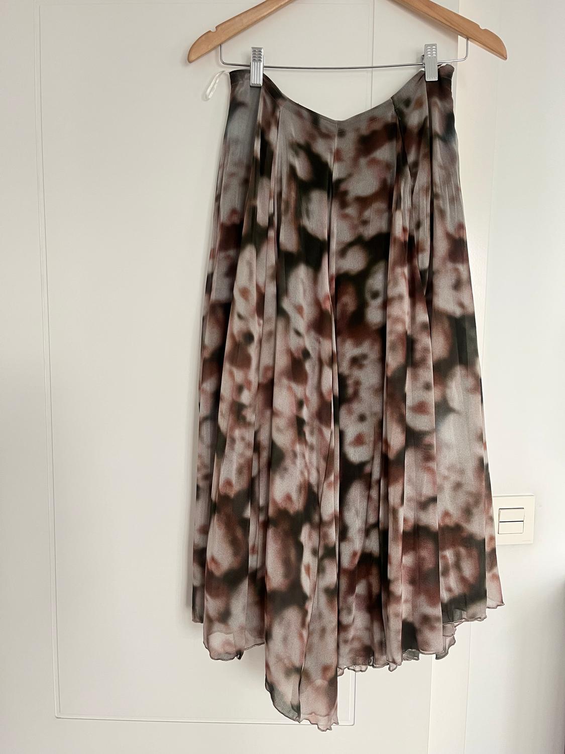 Long skirt with abstract print in brown and black tones, hanging on a wooden hanger against a white wall.