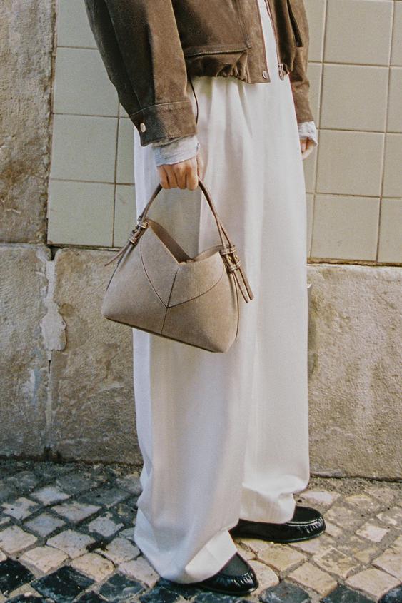 Detail pískovo/hnědé mini shopper kabelky s ručními uchy a odnímatelným ramenním popruhem, kontrastní prošívání.