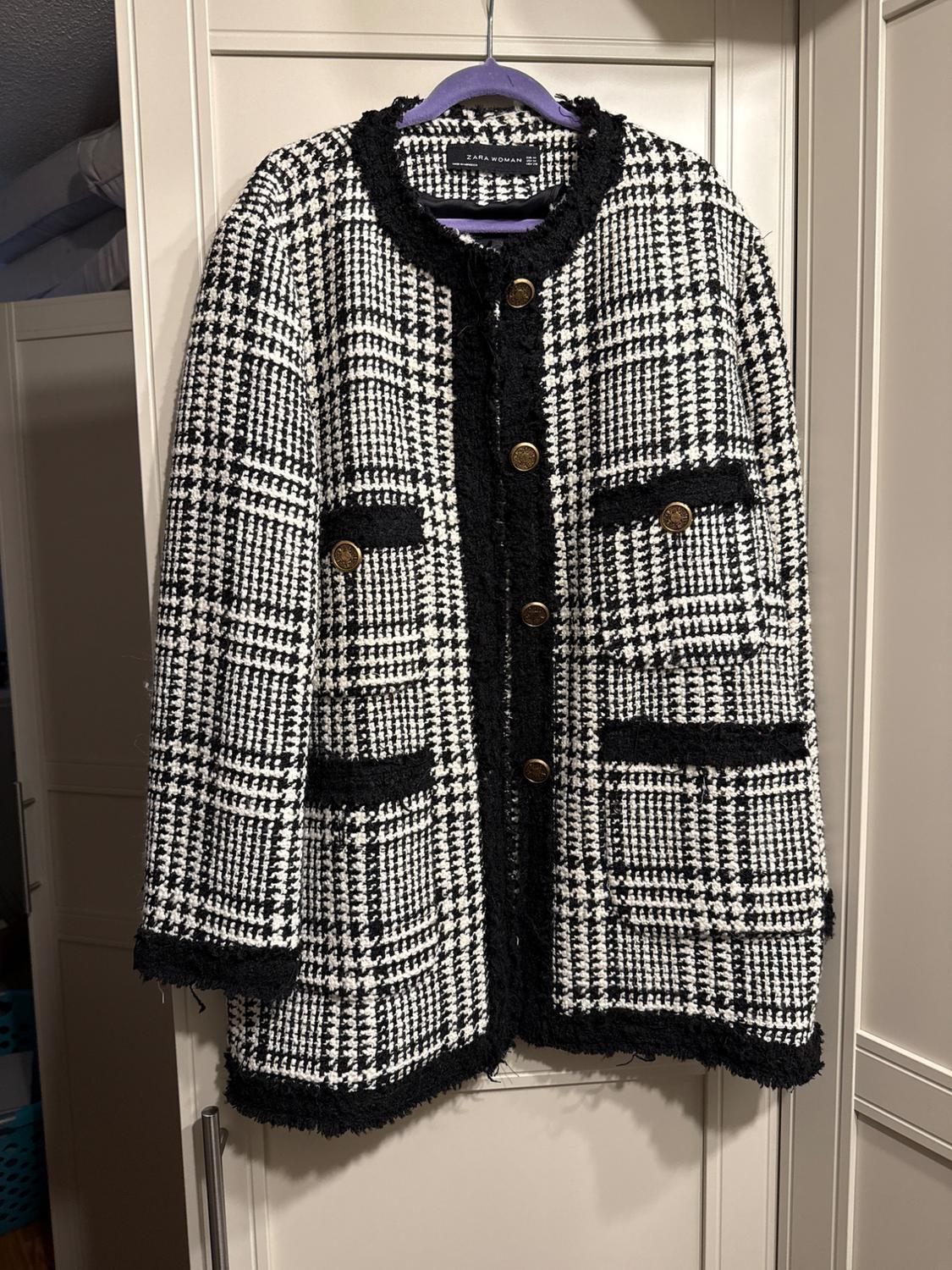 Coat hanging on a hanger, black and white plaid design, with gold buttons and front pockets. "Zara Woman" label.