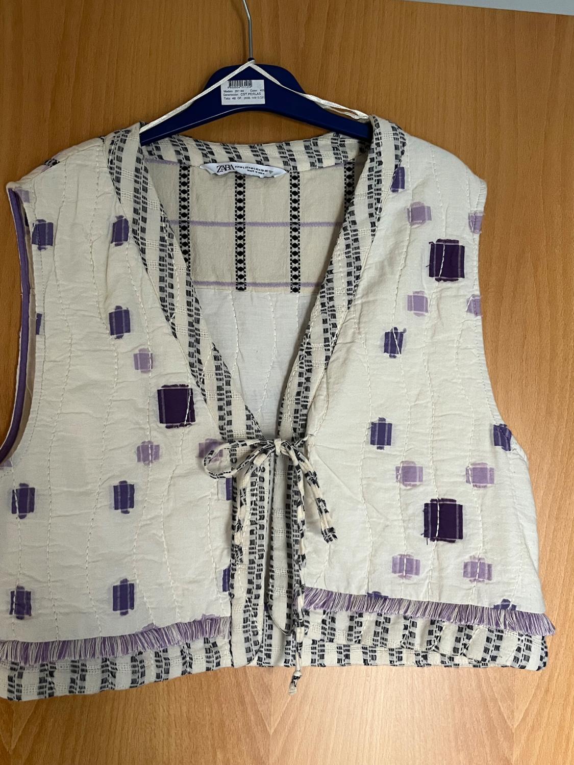 Sleeveless vest with geometric print in shades of purple and black, hanging on a blue hanger over a wooden door.