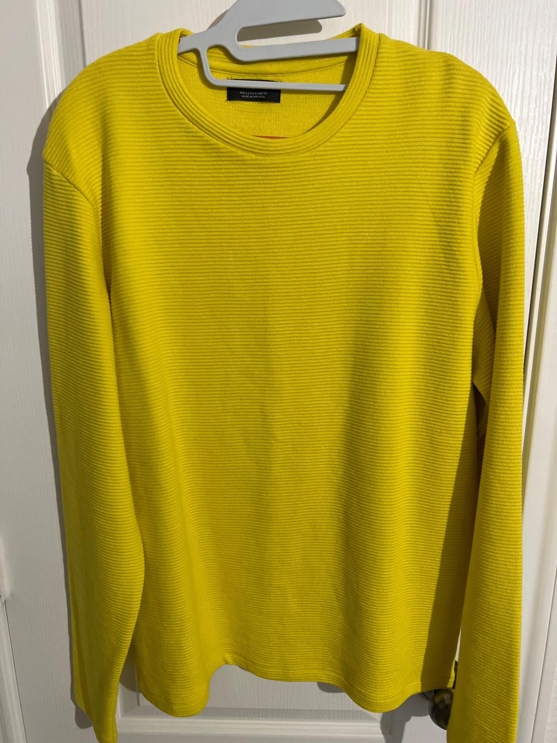 Yellow long-sleeved sweater with a ribbed texture, hanging on a white hanger over a white door.