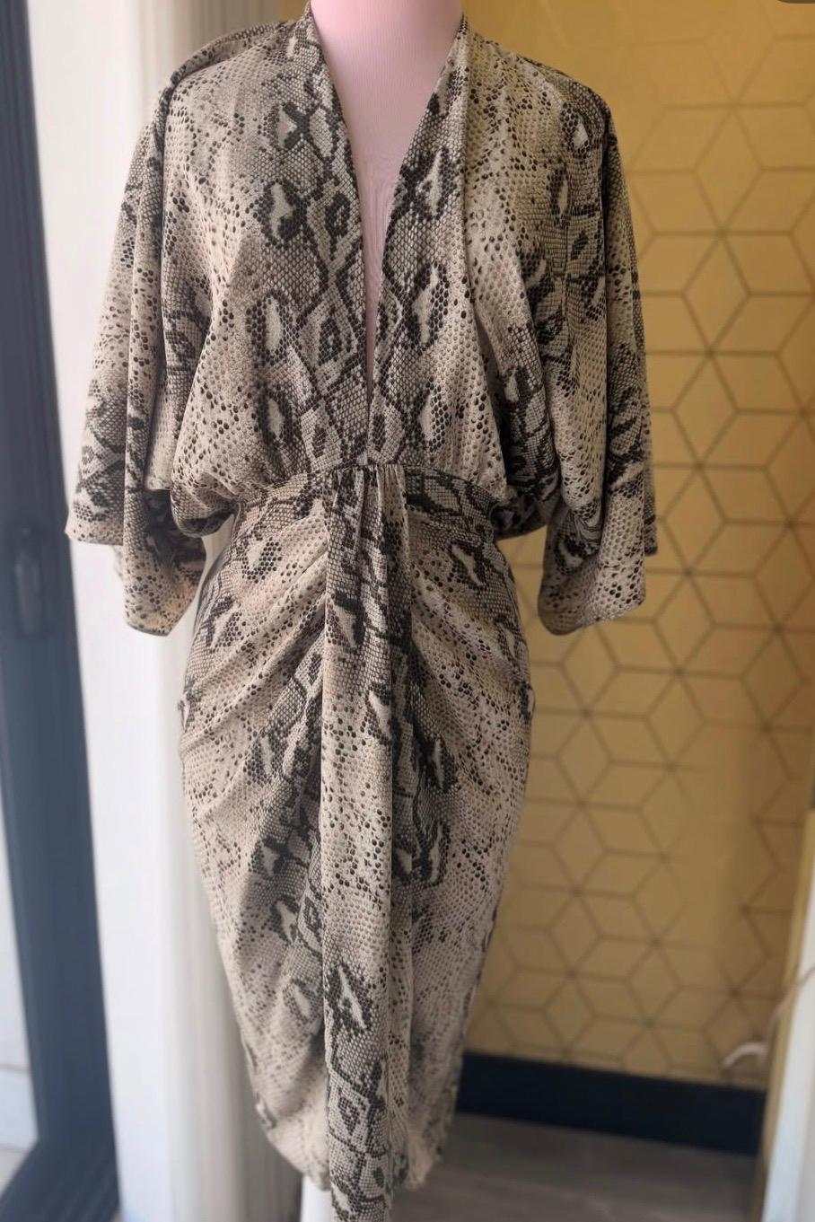 Snake print dress on a pink mannequin, geometric pattern background in beige and black tones.