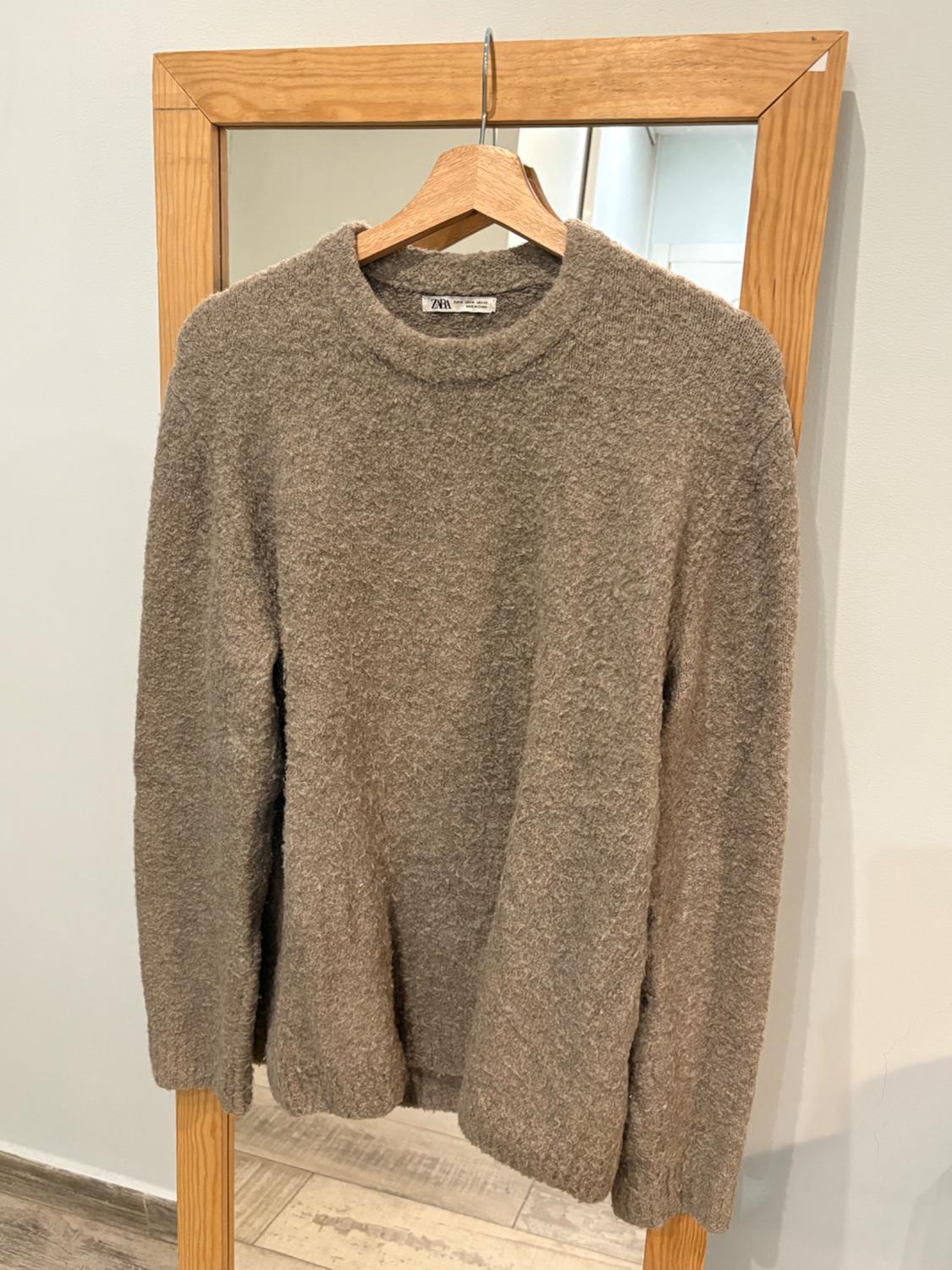 Textured grey jumper hanging on a wooden hanger in front of a wood-framed mirror. Label visible on the neck.