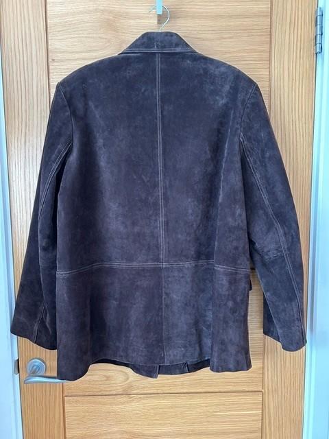 Brown suede jacket hanging on a light wooden door. The jacket is viewed from the back, showing vertical seams.