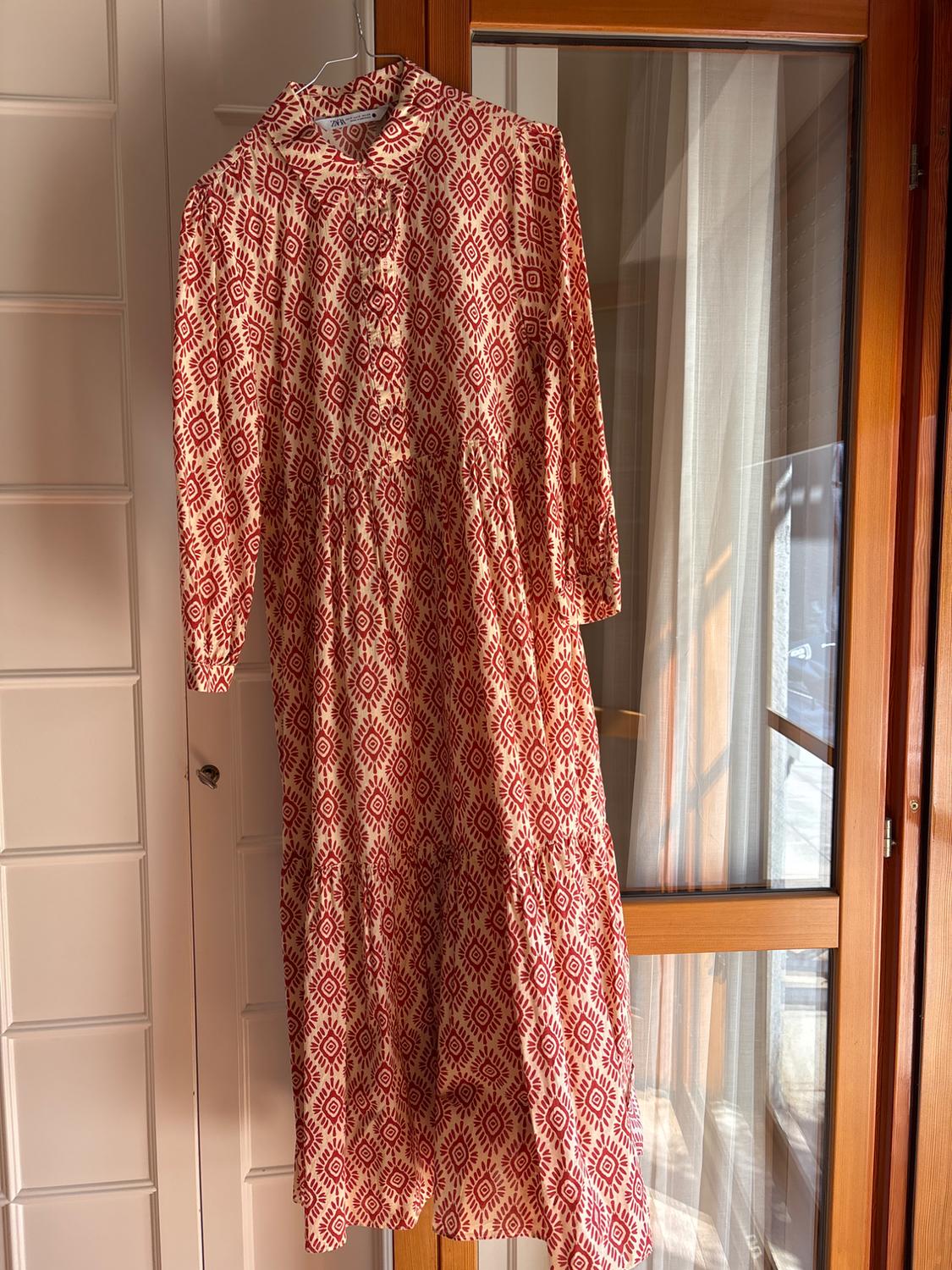 Dress hanging on a wooden door, with a red geometric pattern on a white background. Natural light coming through the window.