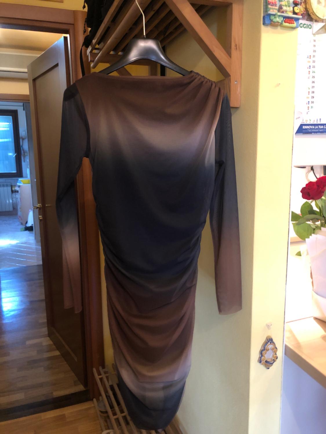 Long-sleeved dress in gradient shades from brown to black, hanging on a black hanger in an interior with a wooden floor.