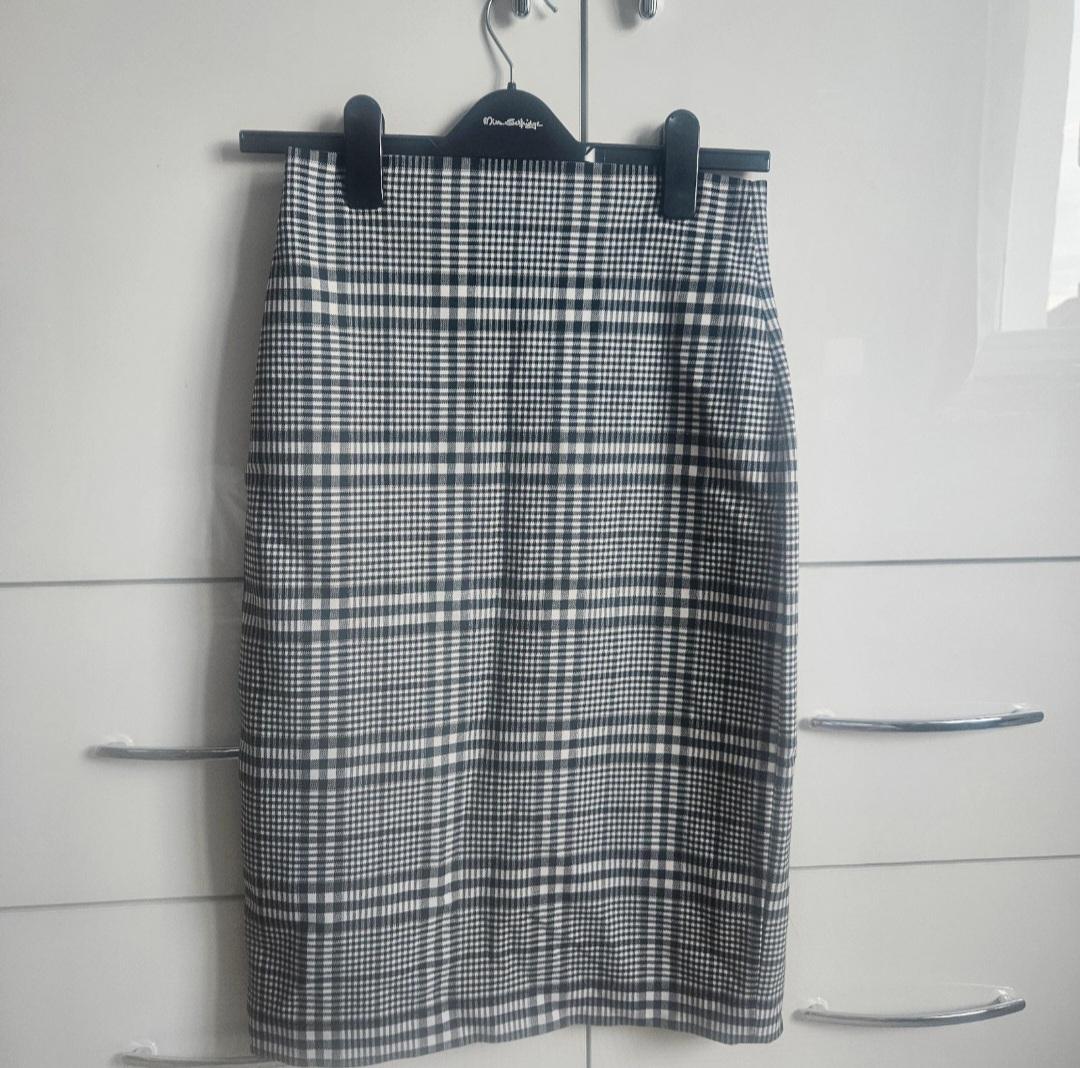 Black and white checked skirt hanging on a black hanger against a white wardrobe background.