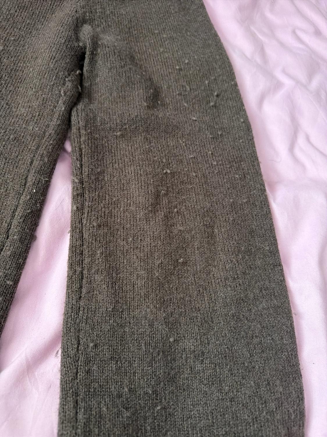 Close-up of a dark grey knitted garment with fuzz on its texture, against a light pink fabric background.