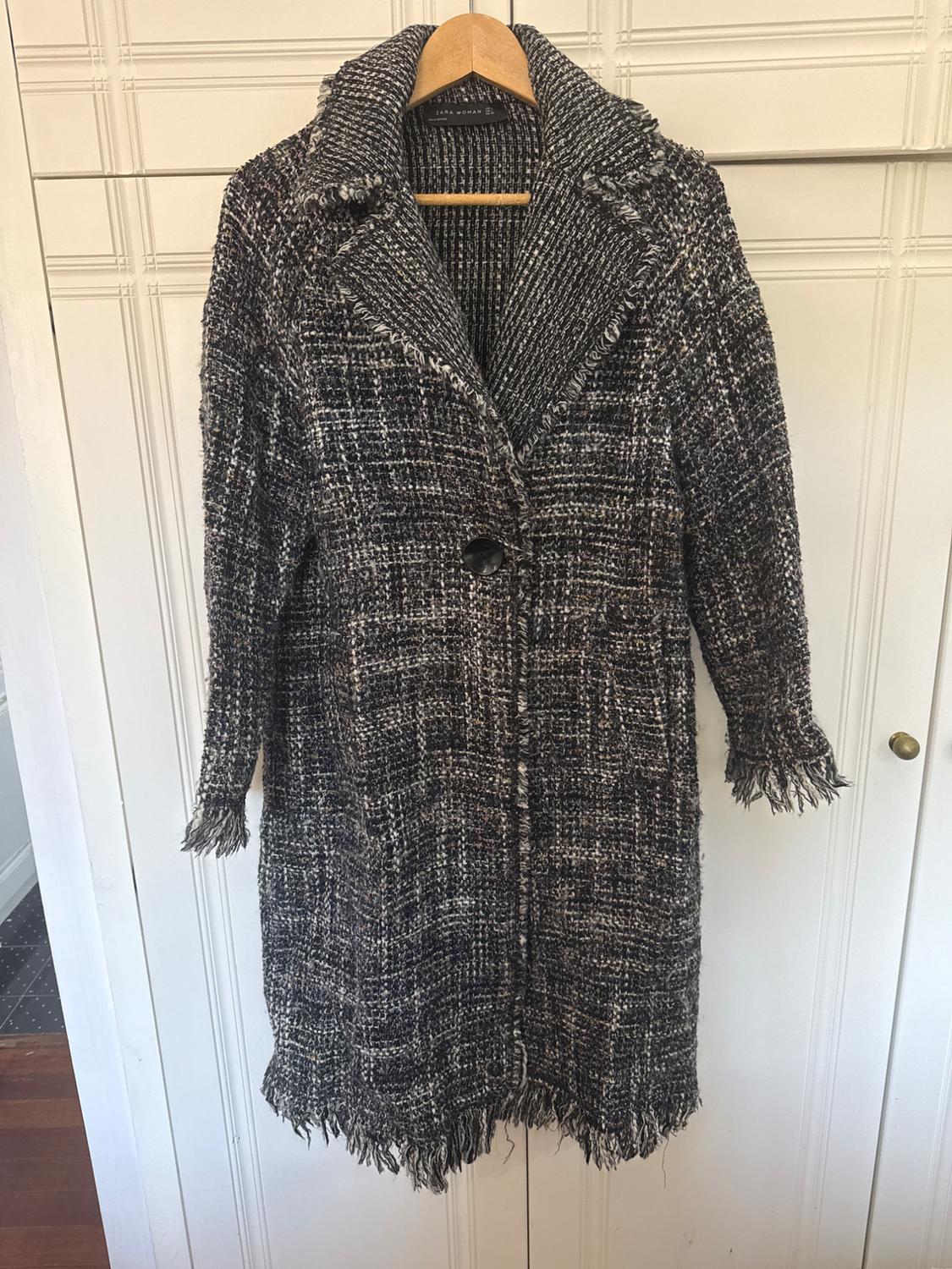 Long coat made from textured fabric in dark shades, hanging on a wooden hanger over a white panelled door.