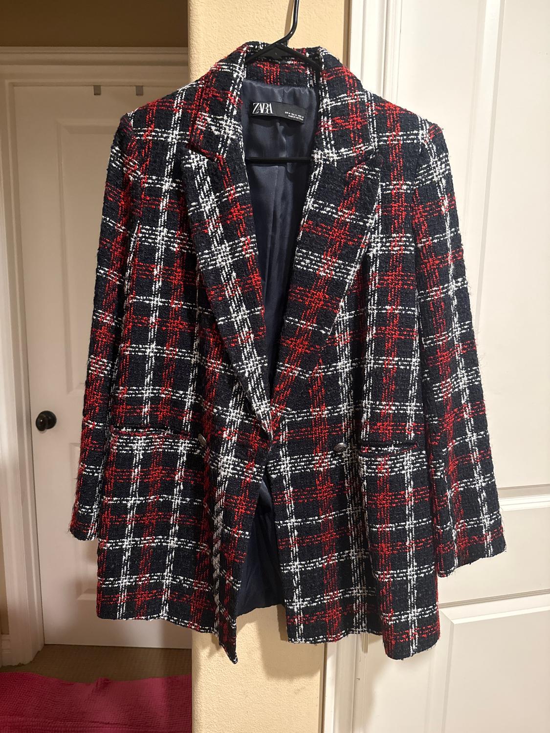 Red, black, and white plaid jacket hanging on a hanger. Visible tag with the ZARA brand. White door background.