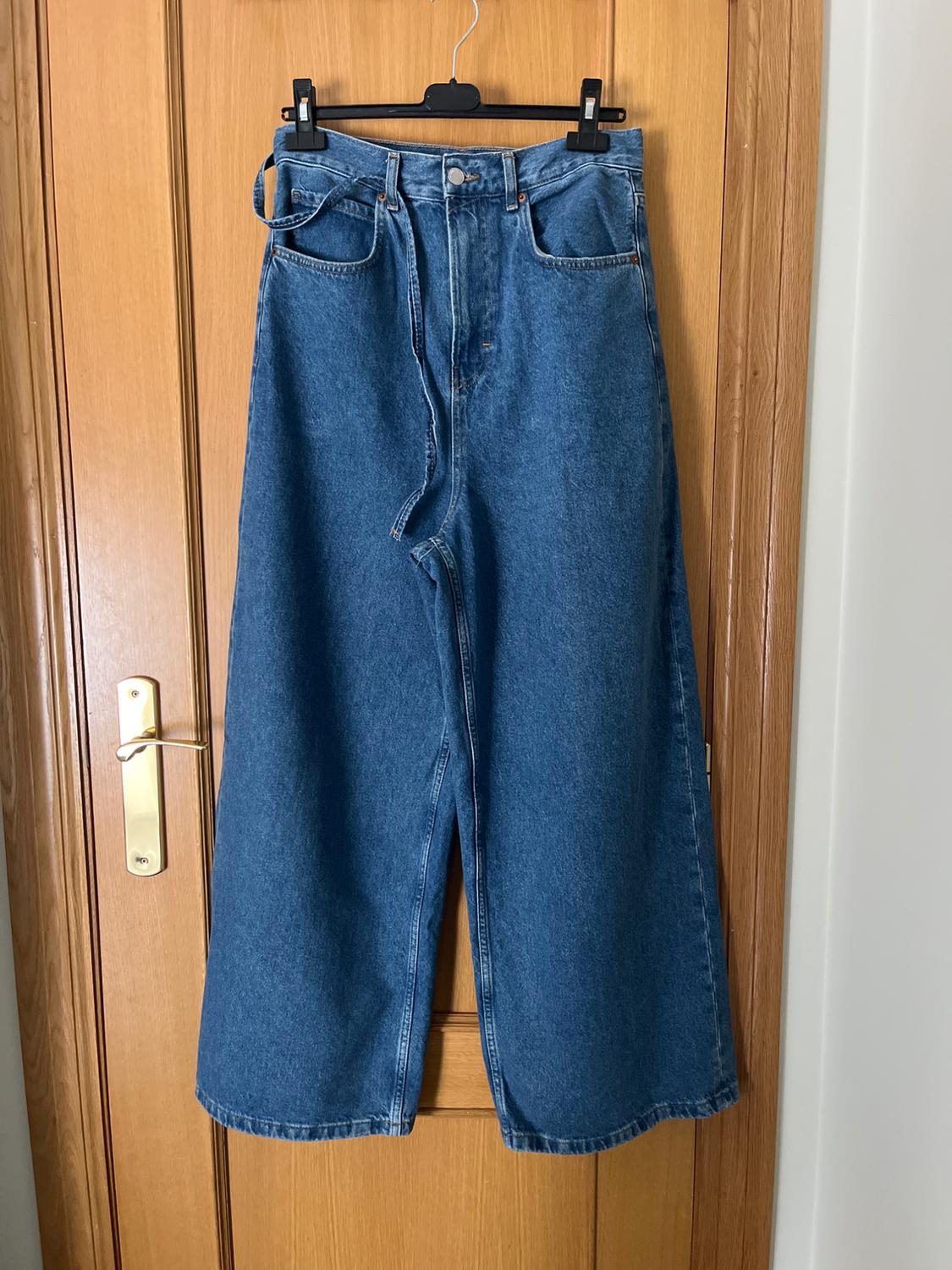 Wide-leg jeans hanging on a black hanger over a light wooden door.