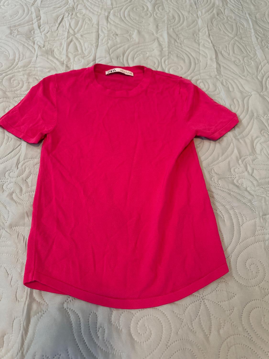 Hot pink short-sleeved casual T-shirt on a textured white bedspread. The label reads ZARA.