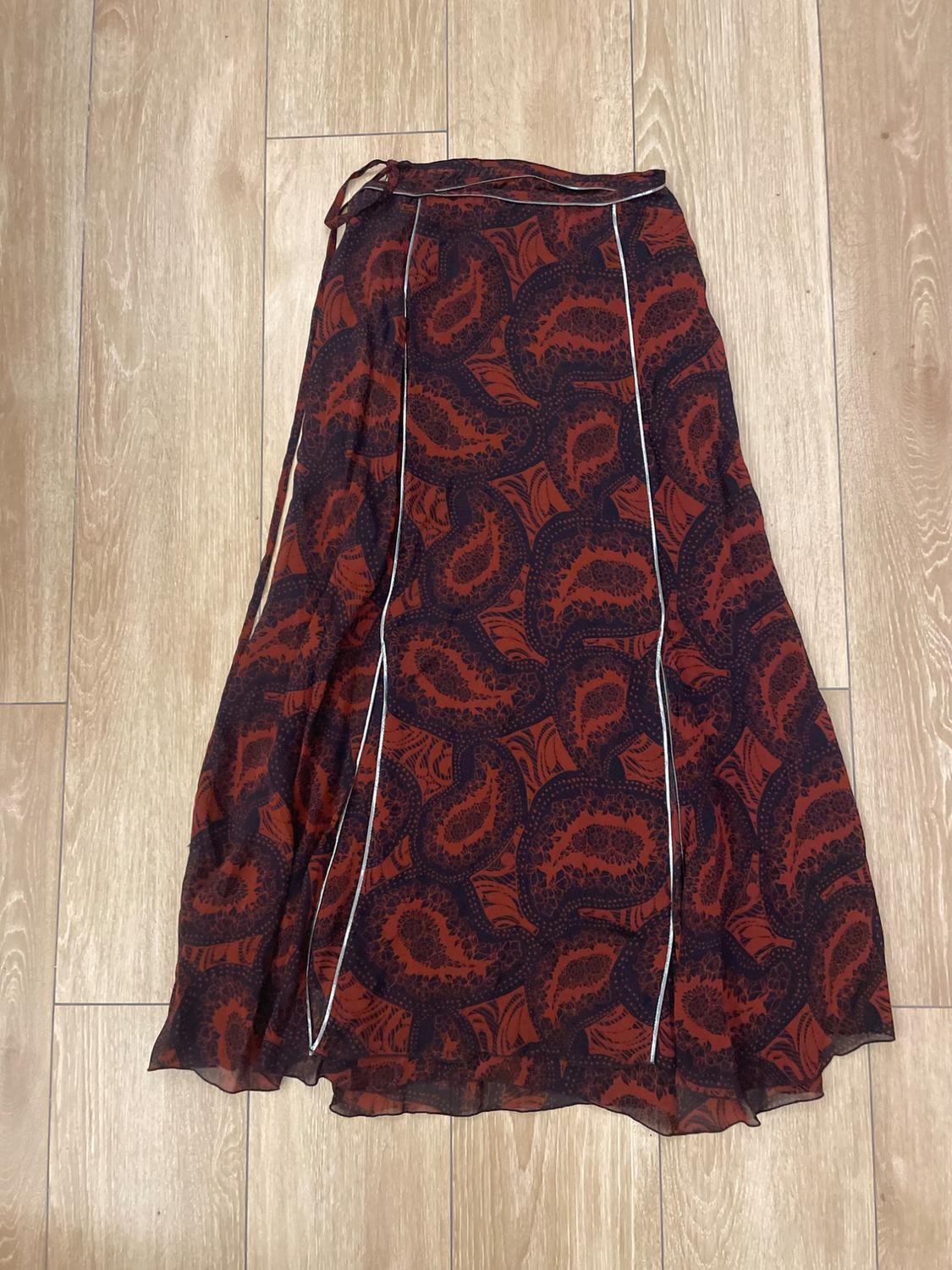 Long skirt with paisley print in brown and black tones, with white line details, on a light wood floor.