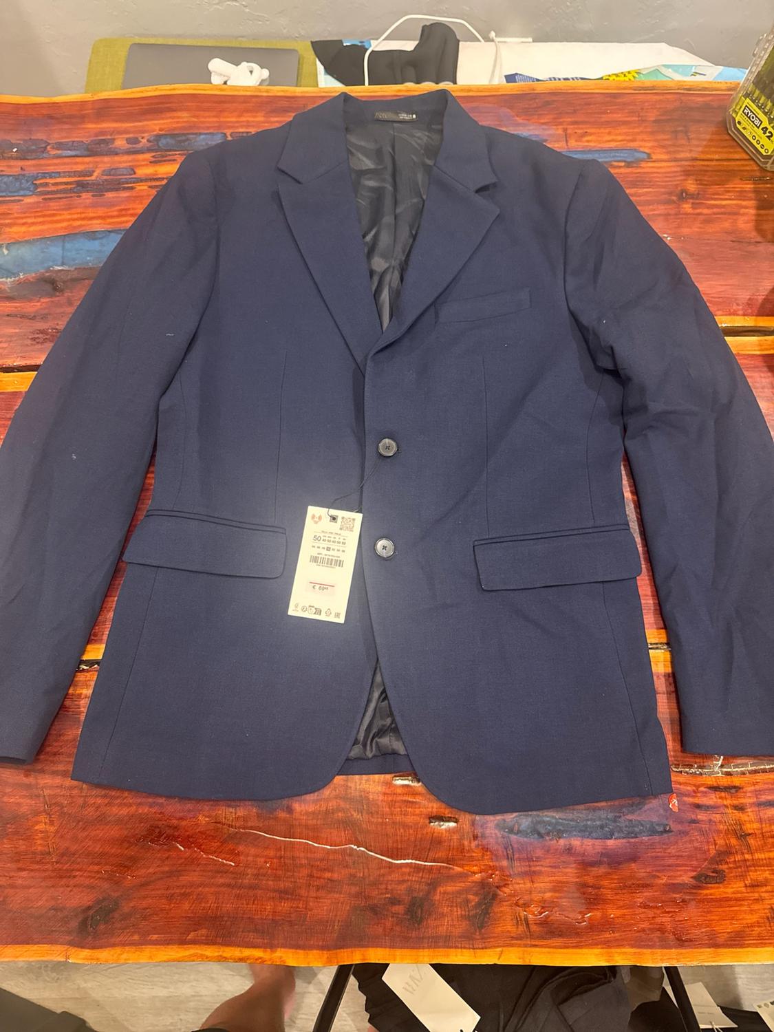 Navy blue two-button blazer on a rustic wooden table. Label with the number 50. Visible text: RYOBI and Zara.