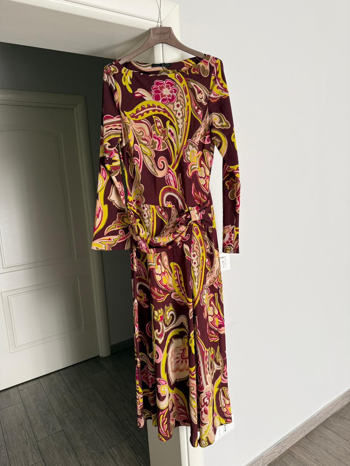 Dress hanging on a hanger with a floral print in shades of brown, yellow, and pink. White wall and white door in the background.