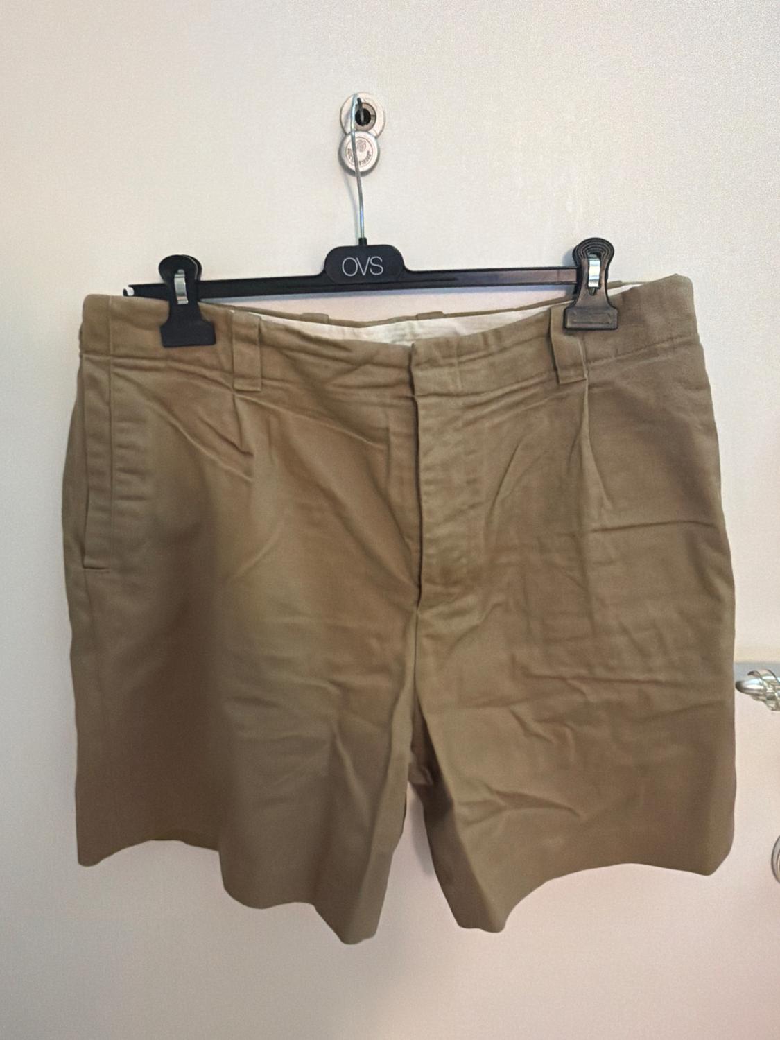 Casual-style beige shorts hanging on a black hanger with the text OVS on a white door.