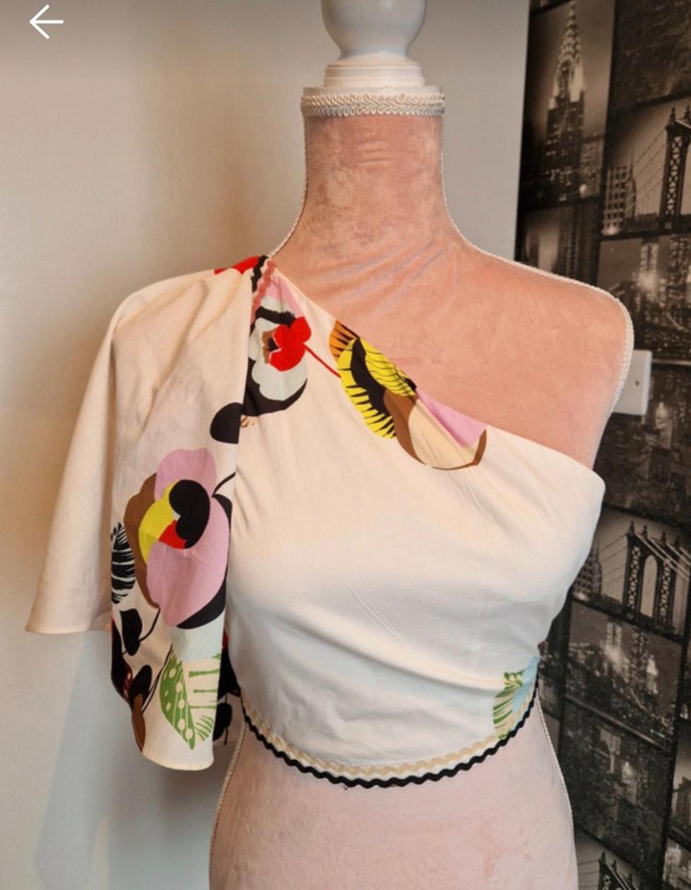 White asymmetric top with a colourful floral print on a mannequin, with a background of black and white photos of buildings.