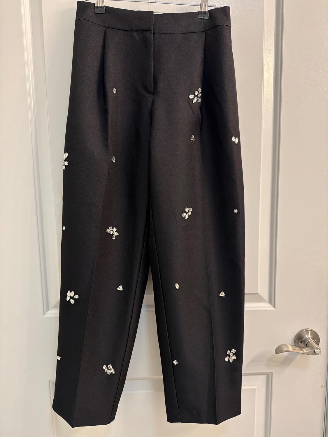 Black pants hanging on a white door, decorated with small, sparkling embellishments distributed throughout the garment.