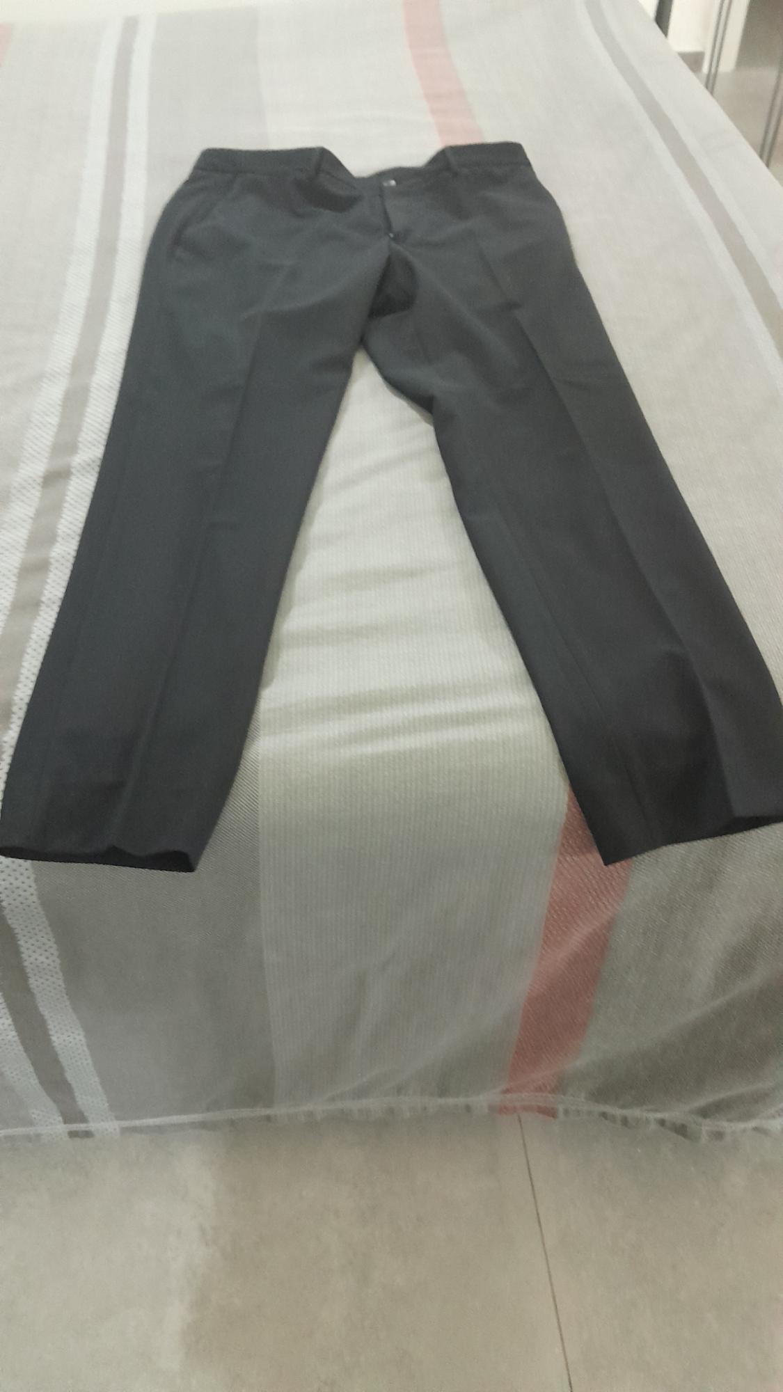 Black smart trousers laid out on a bed with a grey and red striped bedspread, in a brightly lit indoor setting.