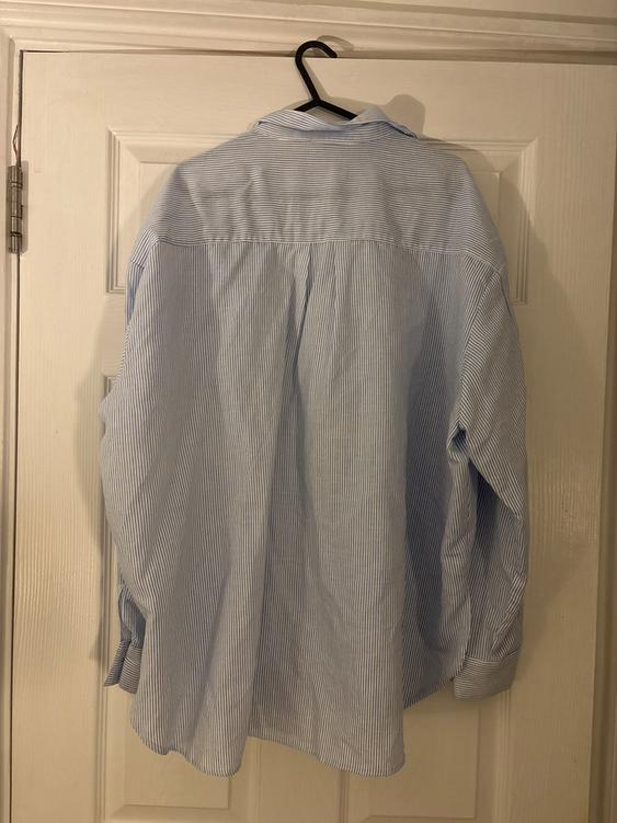 Blue and white striped shirt hanging on a black hanger over a white door. Rear view of the garment.