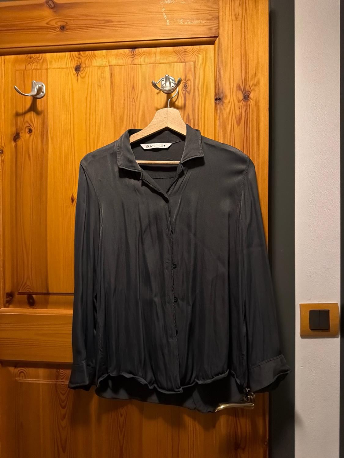 Black button-up long-sleeved shirt hanging on a wooden hanger over a door. Label bearing the text ZARA.