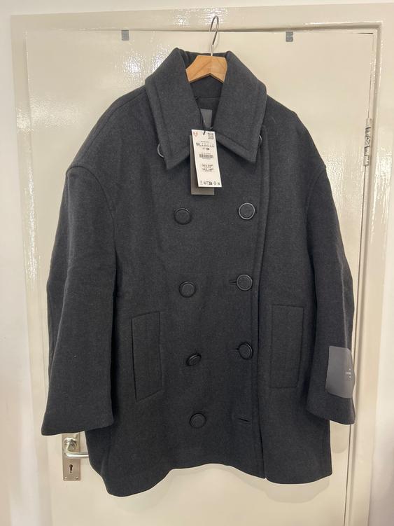 Dark grey wool coat hanging on a wooden hanger, with large buttons and a visible label on the front.