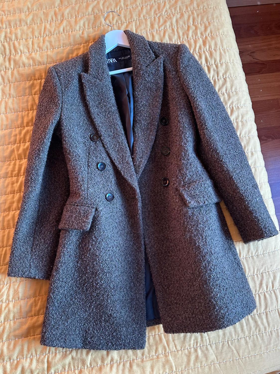 Textured grey double-breasted coat on a yellow quilt. Visible label on collar.