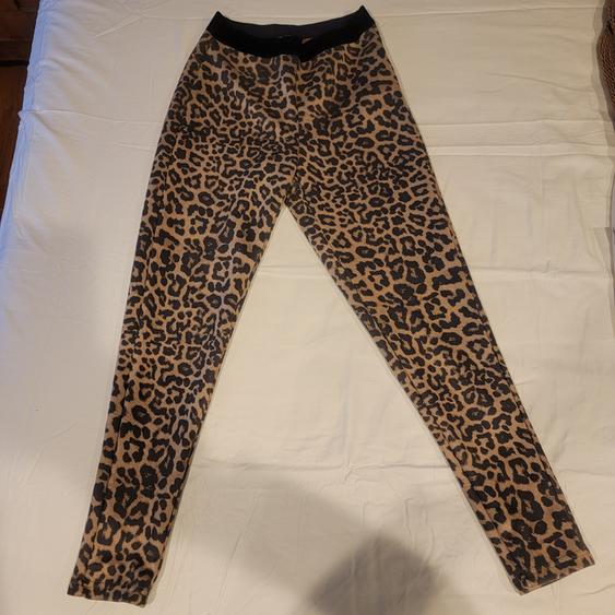 Form-fitting leopard print pants on a white bed. Black elastic waistband. Modern and daring style.