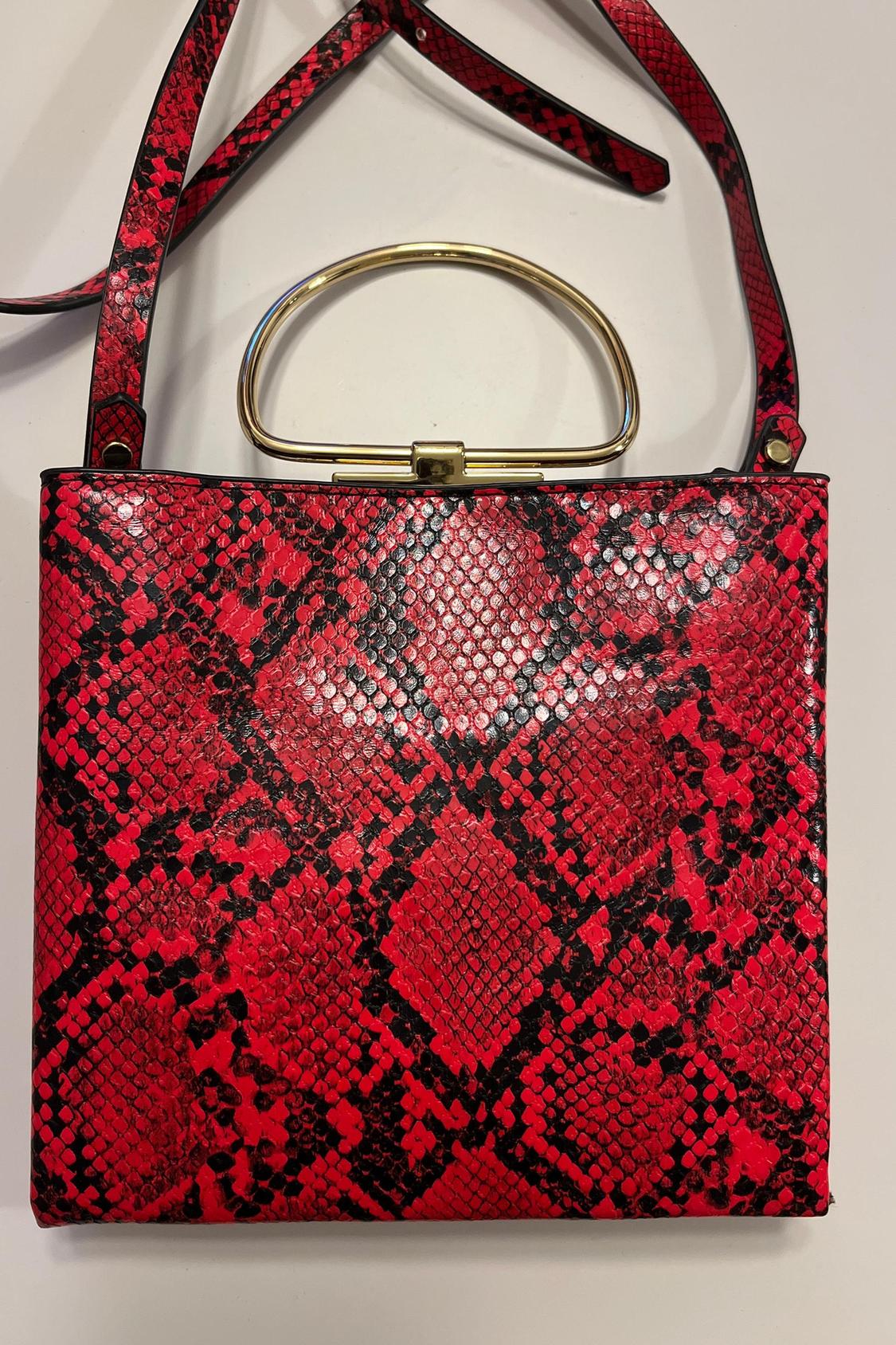 Close-up of red handbag with snake print and gold metallic handle.