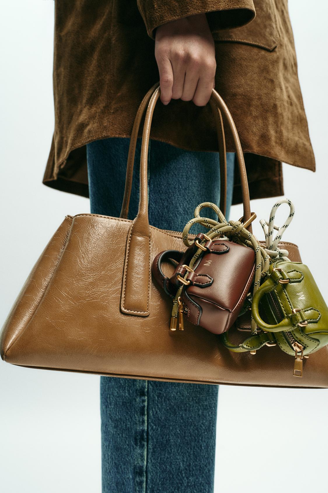 Srednji posnetek rjave torbice z ročaji, okrašene z mini torbicami v rjavi in zeleni barvi, na belem ozadju.