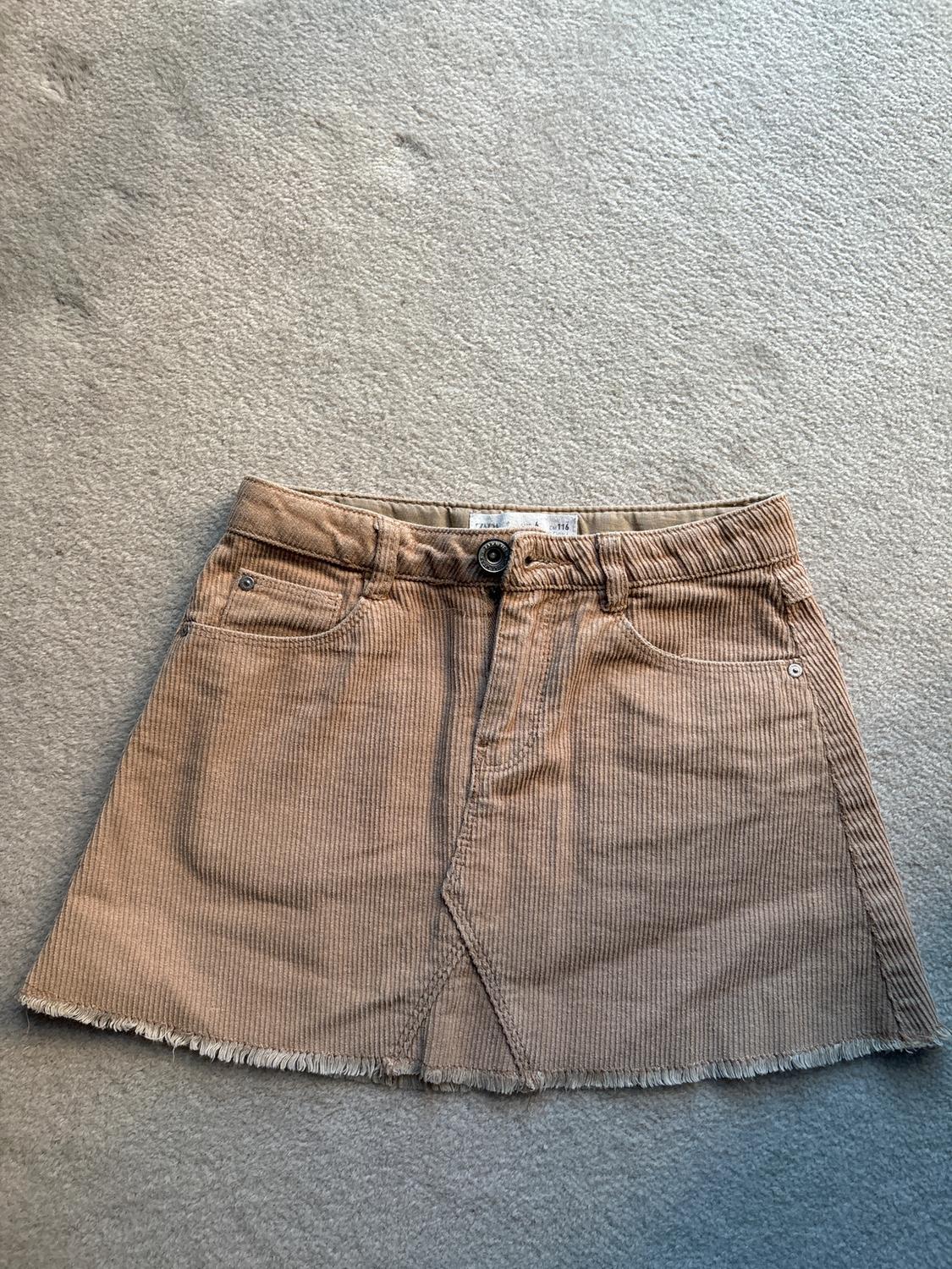 Light brown corduroy mini skirt with front pockets and frayed hem, on a beige carpet.