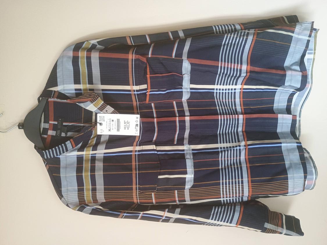 Checked shirt in shades of blue, white, and brown, hanging on a hanger. Visible tag with product details.