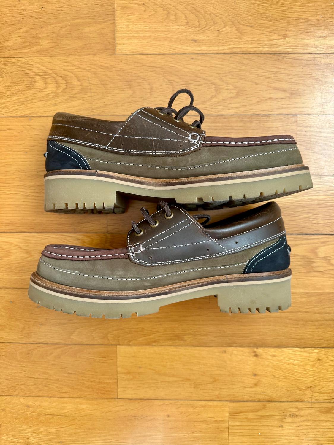 Brown leather shoes with thick soles and white stitching, placed on a light wooden floor.