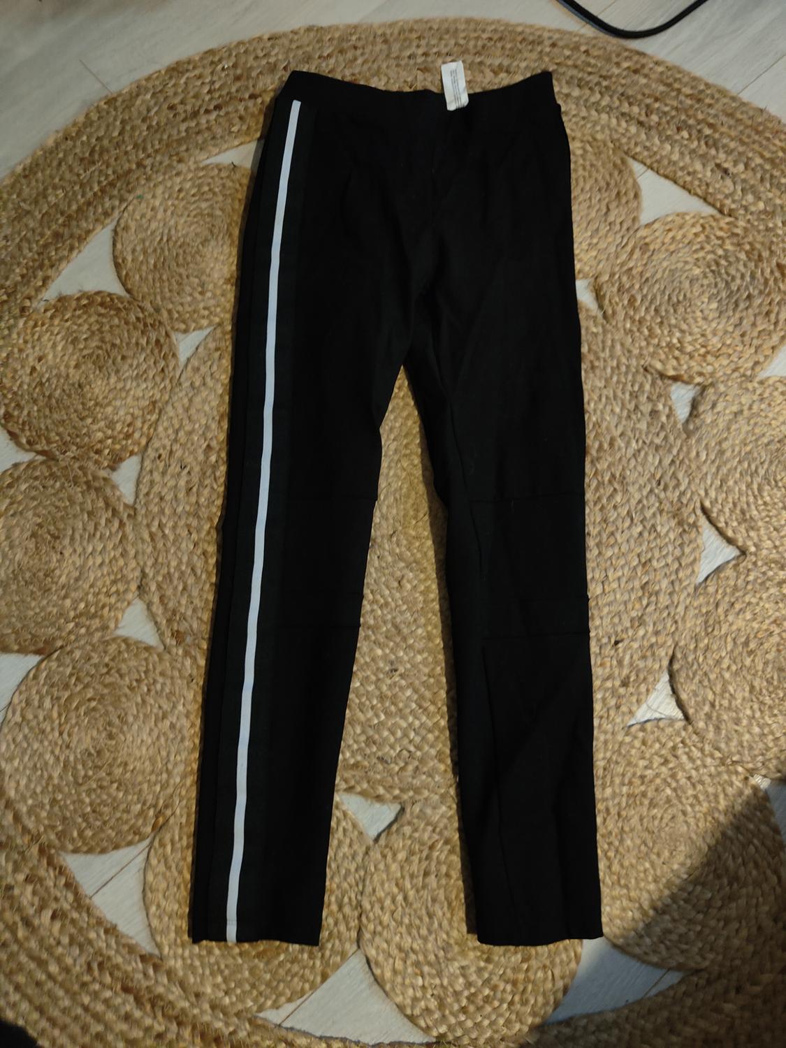 Black trousers with a white stripe on the left side, placed on a spirally braided jute rug.