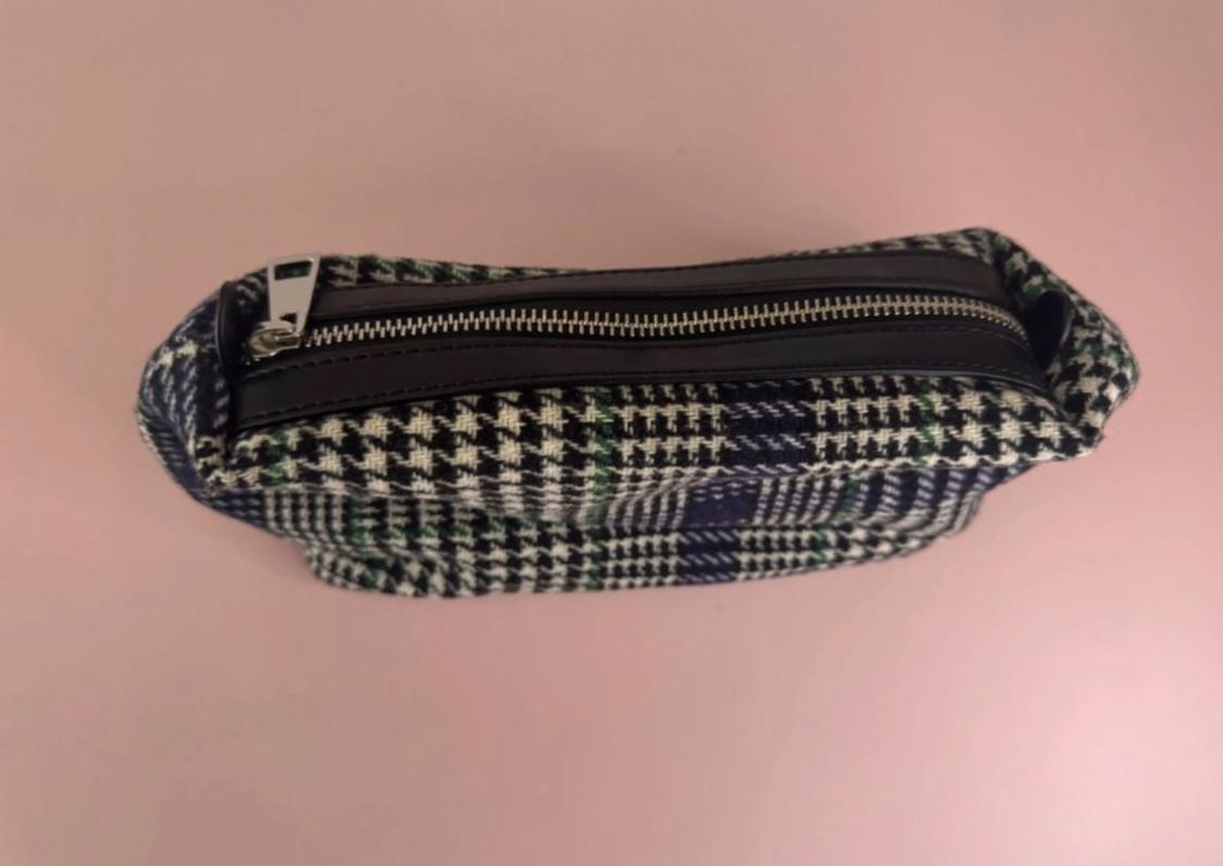 Black and white checked fabric bag, with a metallic zip closure, on a light pink background.