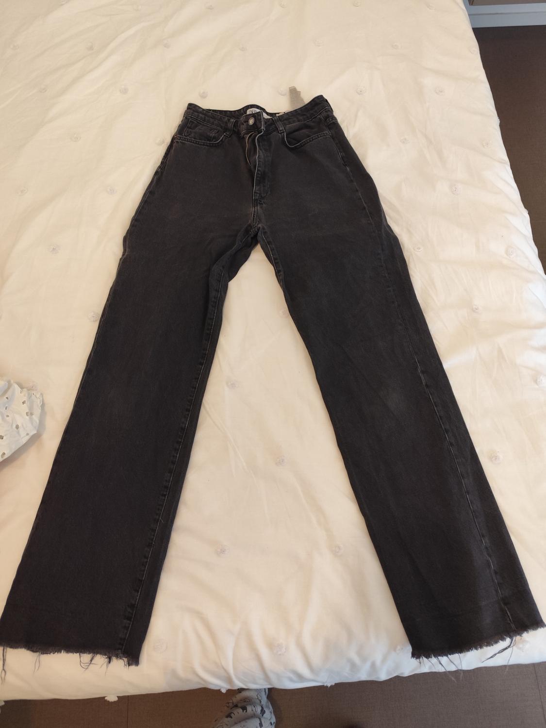 Black, straight-cut jeans with a frayed hem, placed on a white quilted bedspread.