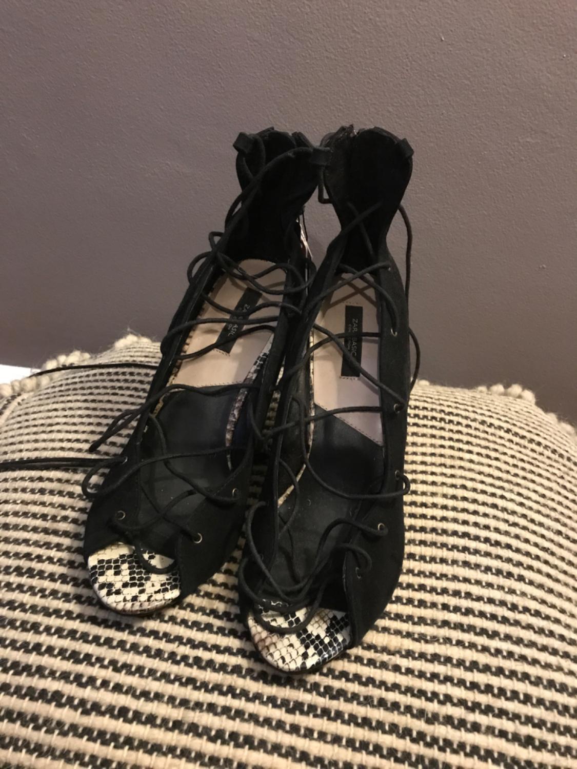 Black heeled shoes with laces and a snakeskin print detail on the toe.