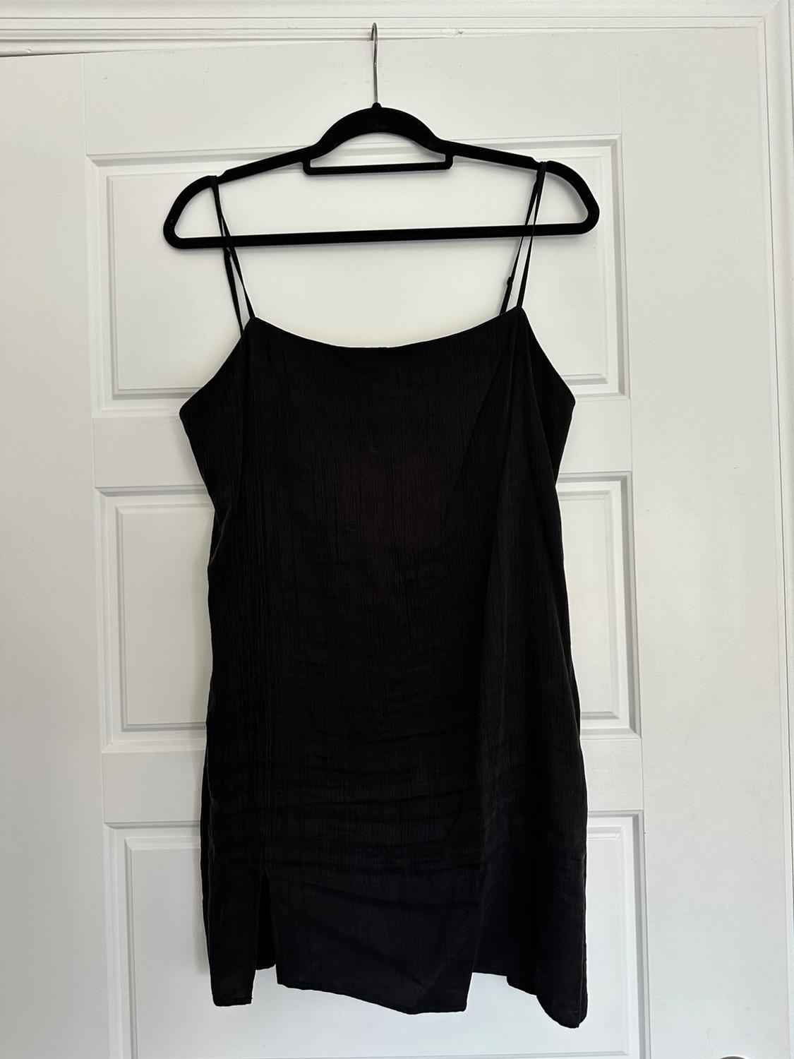 Black slip dress hanging on a black coat hanger in front of a white door with rectangular panels.