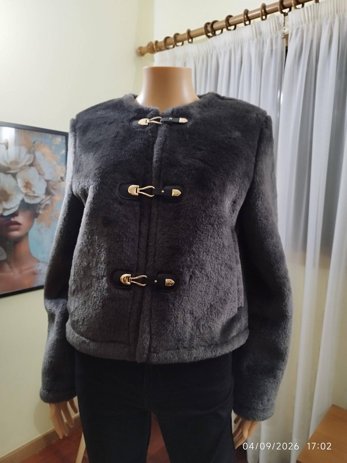 Mannequin wearing a grey fur jacket with gold fastenings and black trousers indoors with a painting. Text: 04/09/2026 17:02.