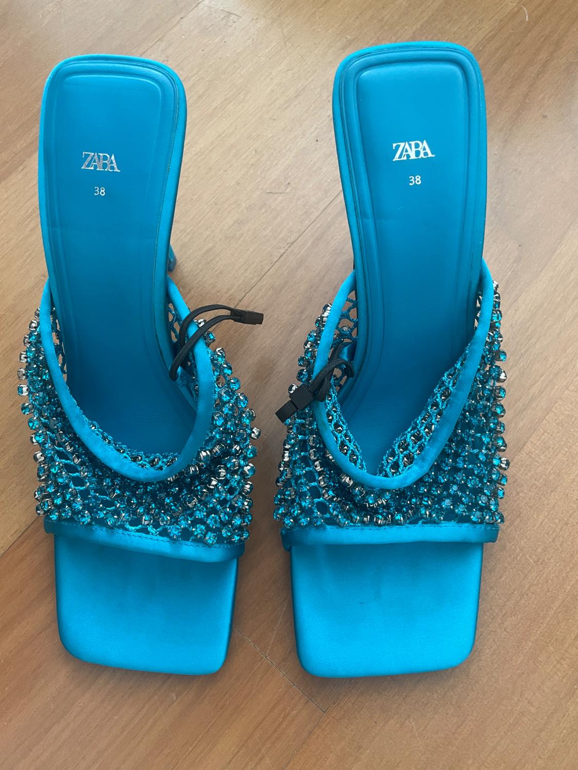 Blue sandals with embellishments and a block heel on a wooden floor. Visible text: "ZARA 38".