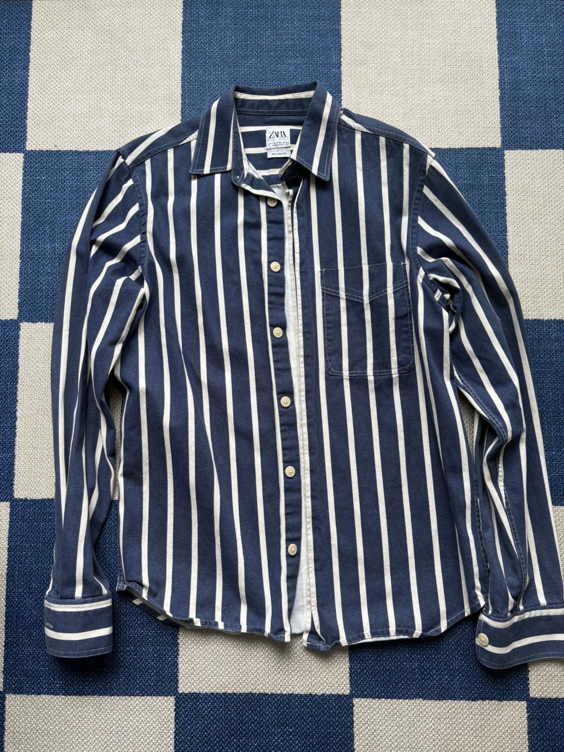 Blue and white vertical striped shirt on a blue and white checkered rug. Visible tag with text "ZARA".