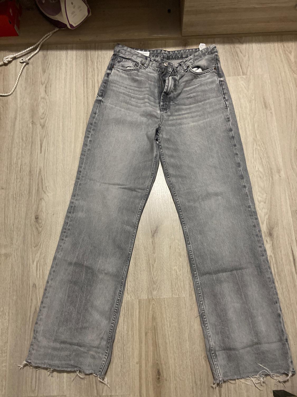 Wide-leg grey jeans with a frayed hem, laid on a light wooden floor.