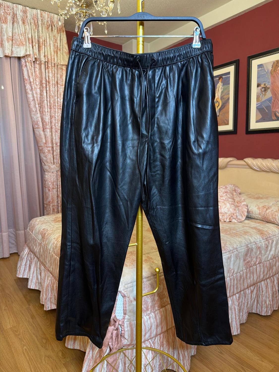 Black trousers hanging on a gold hanger in a bedroom with pink curtains and bedspread. Background with pictures on the wall.