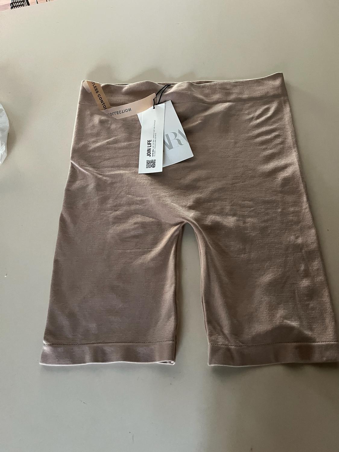 Beige cycling shorts on a light-coloured surface. Includes labels with the text JOIN LIFE. Casual and comfortable style.