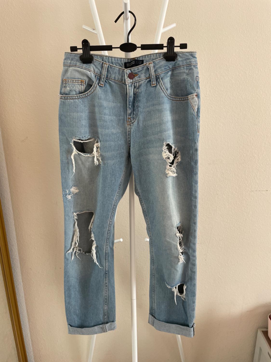 Front view of distressed blue jeans with rips on the legs and visible front pockets.