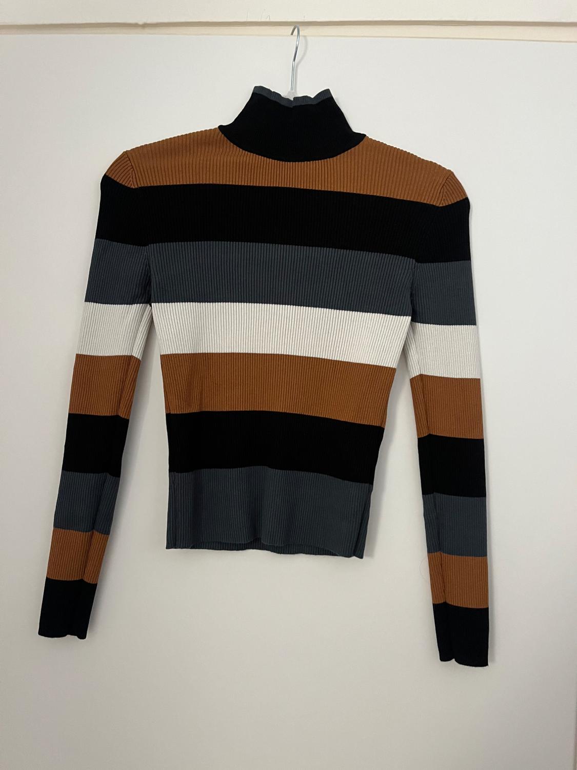 High-neck jumper with horizontal stripes in black, brown, grey, and white, hanging on a hanger against a white background.